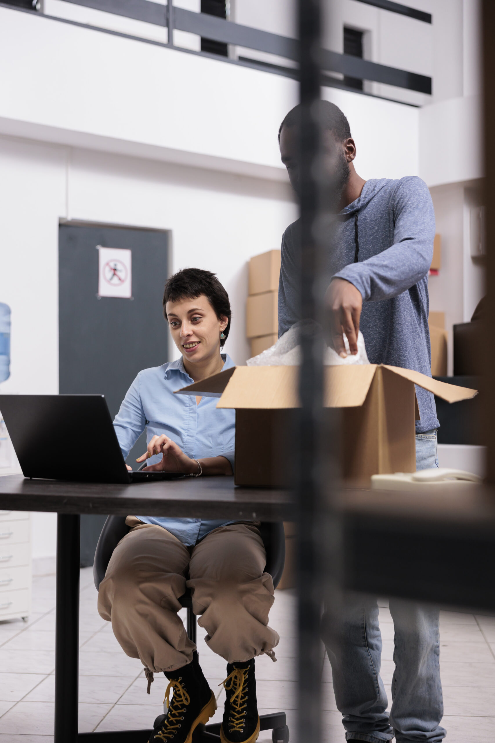 Woman using laptop while man unpacks cardboard box nearby Woman using laptop while man unpacks cardboard box nearby
