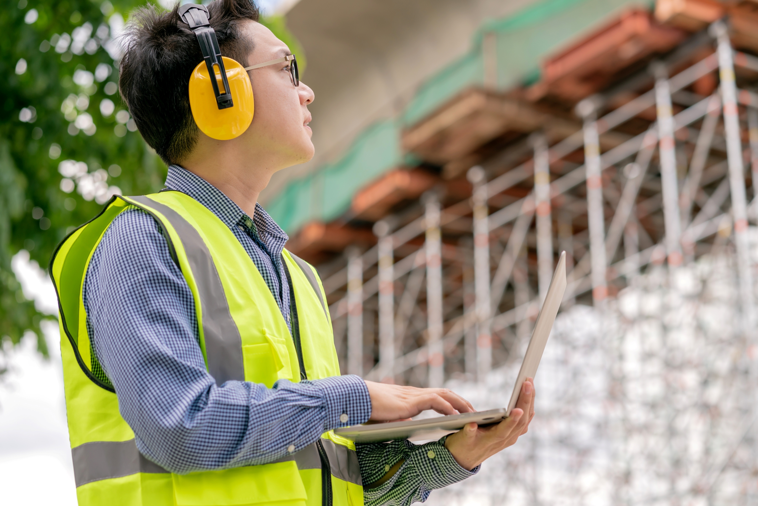 Man wearing ear muffs using laptop at construction site Man wearing ear muffs using laptop at construction site