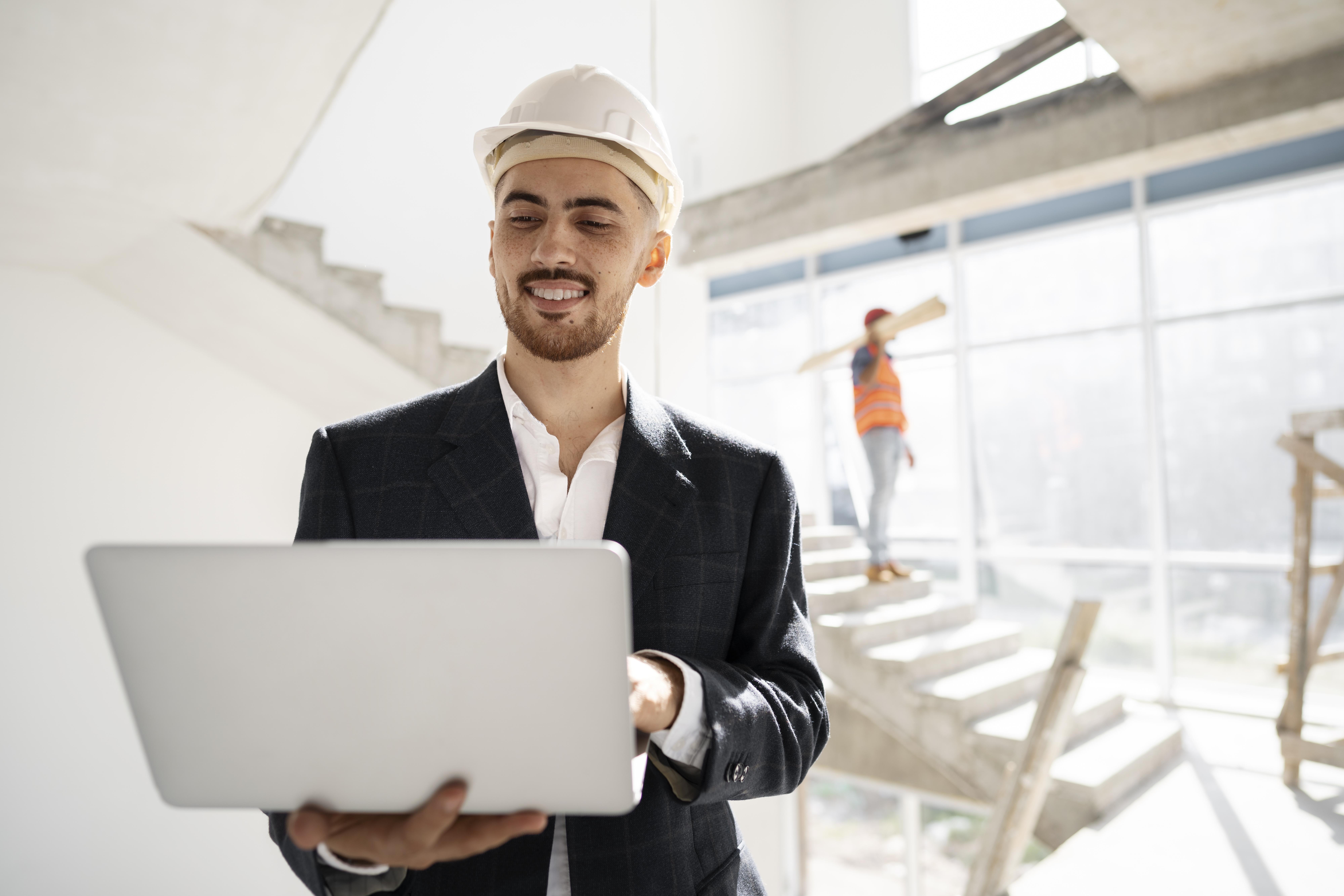 Engineer wearing hard hat using laptop at construction site