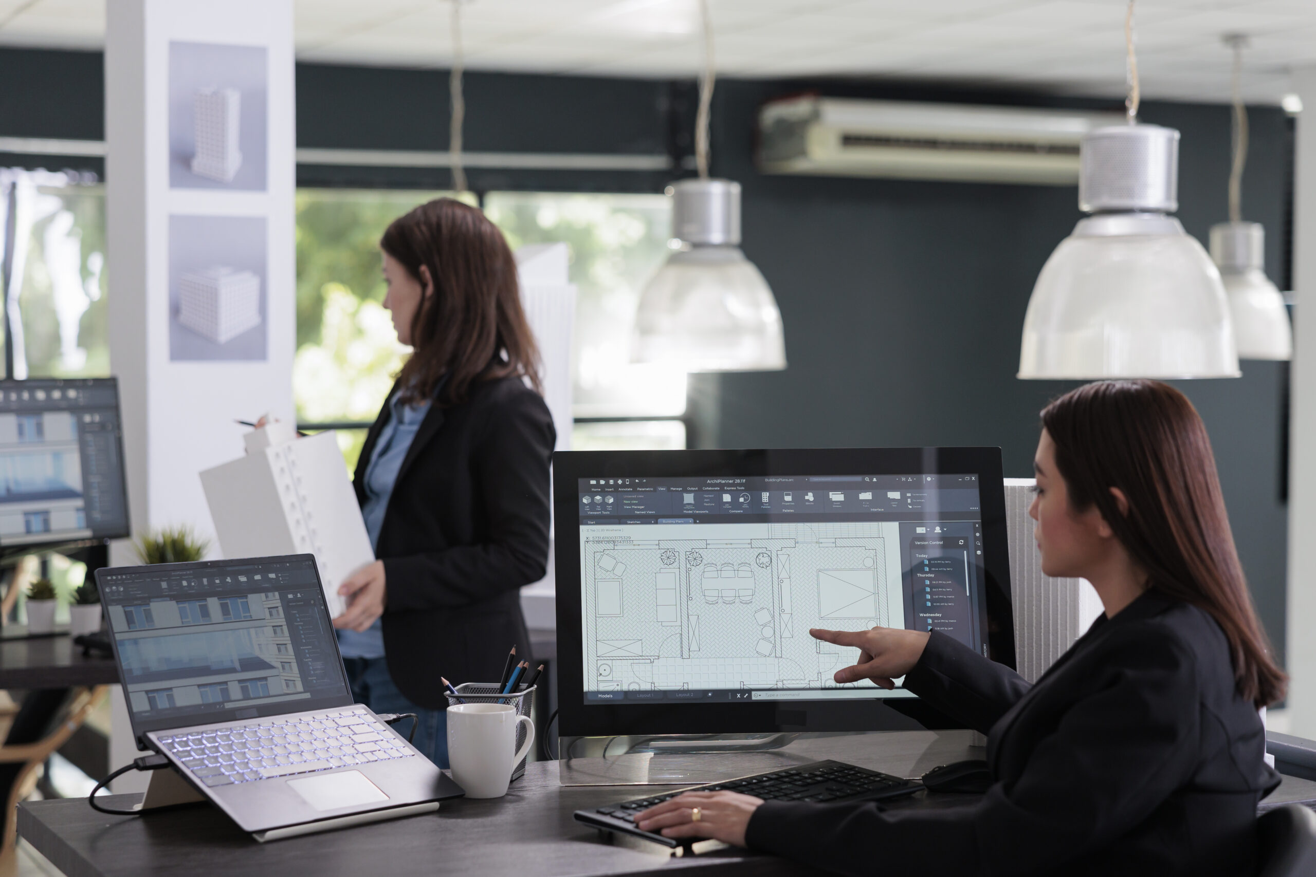 Architect reviewing floor plans on monitor Architect reviewing floor plans on monitor, colleague standing in the background