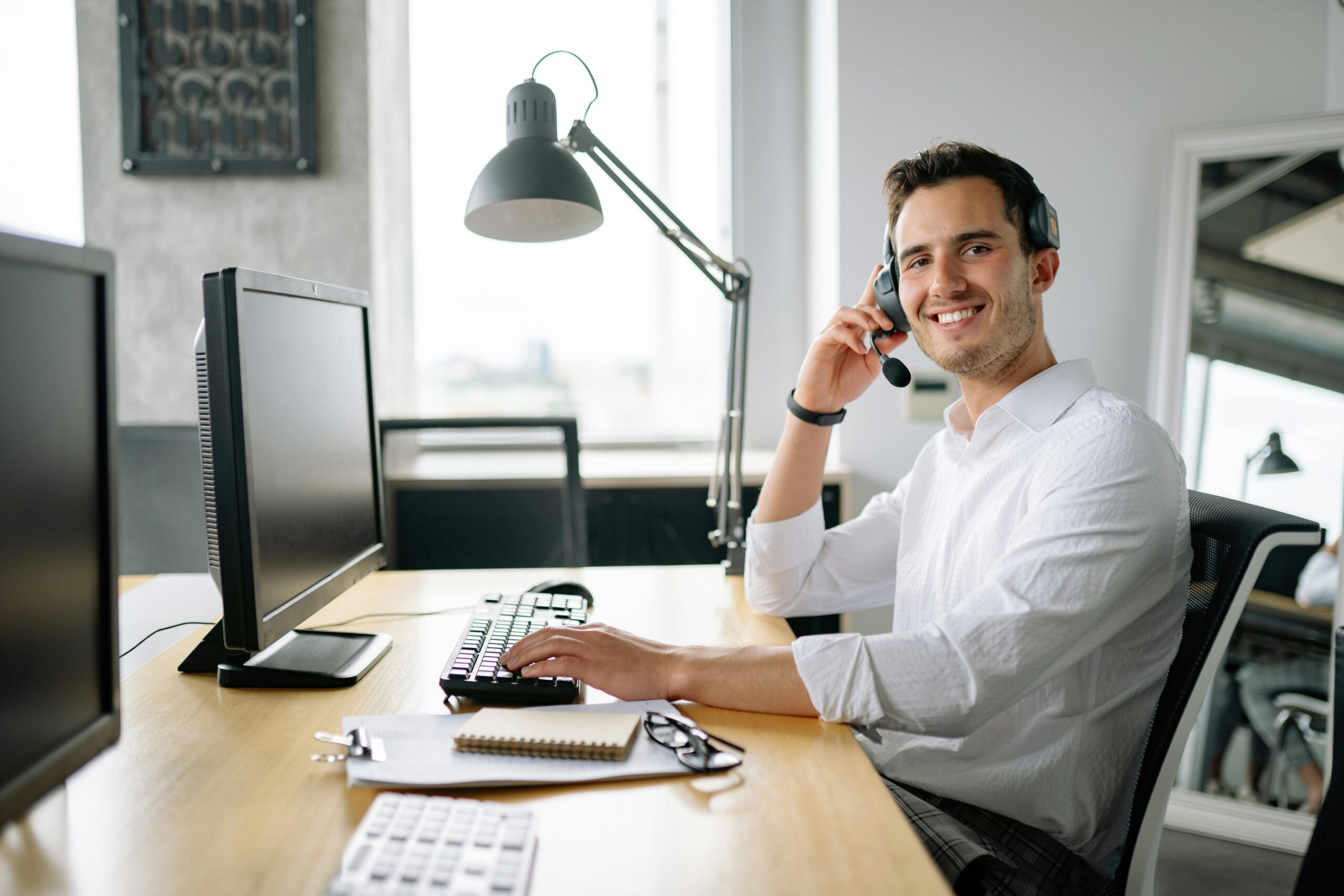 IT support specialist smiling while holding headphones in front of work station IT support specialist smiling while holding headphones in front of work station