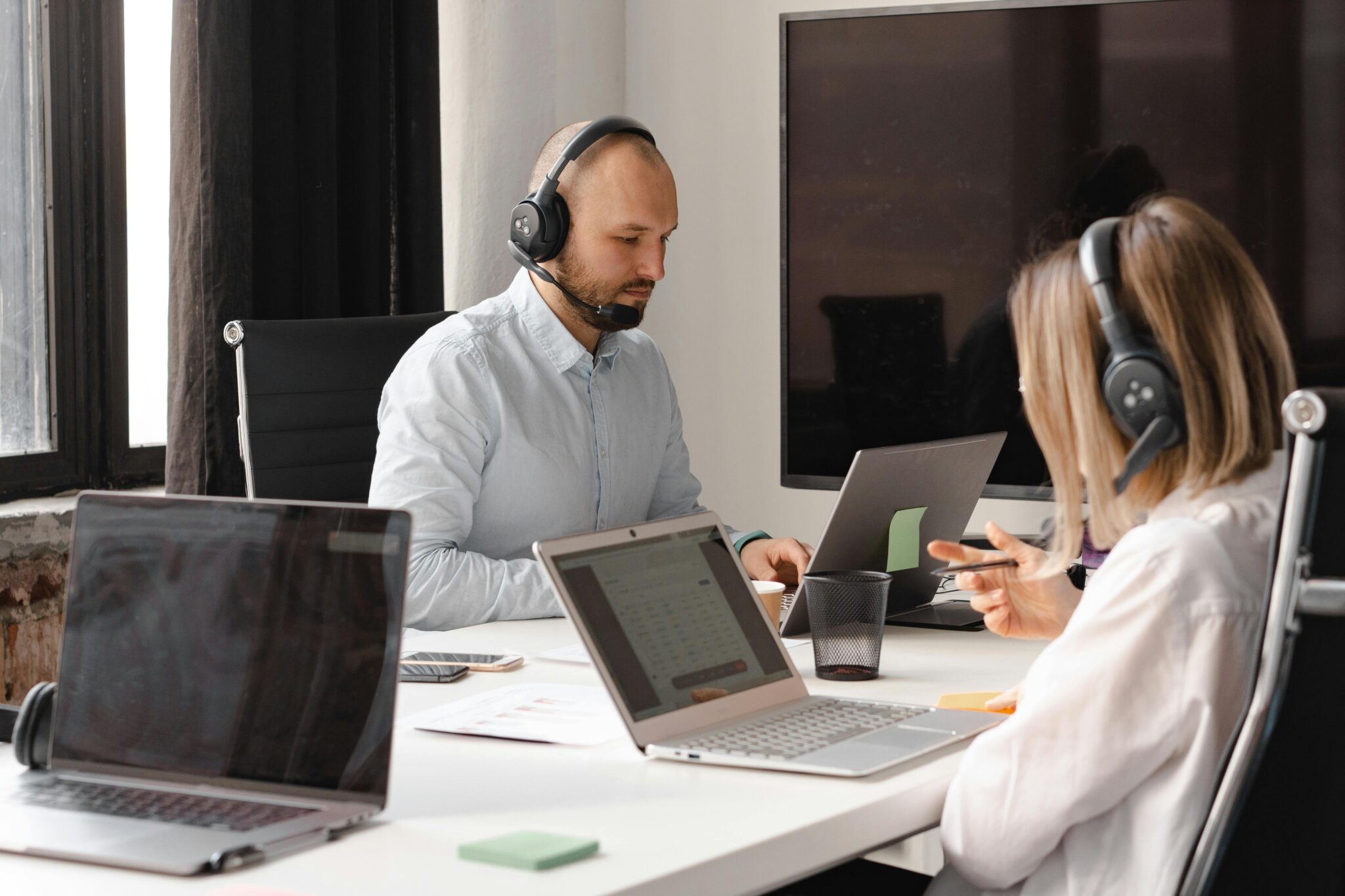 Two people in front of laptops wearing headphones with microphones.